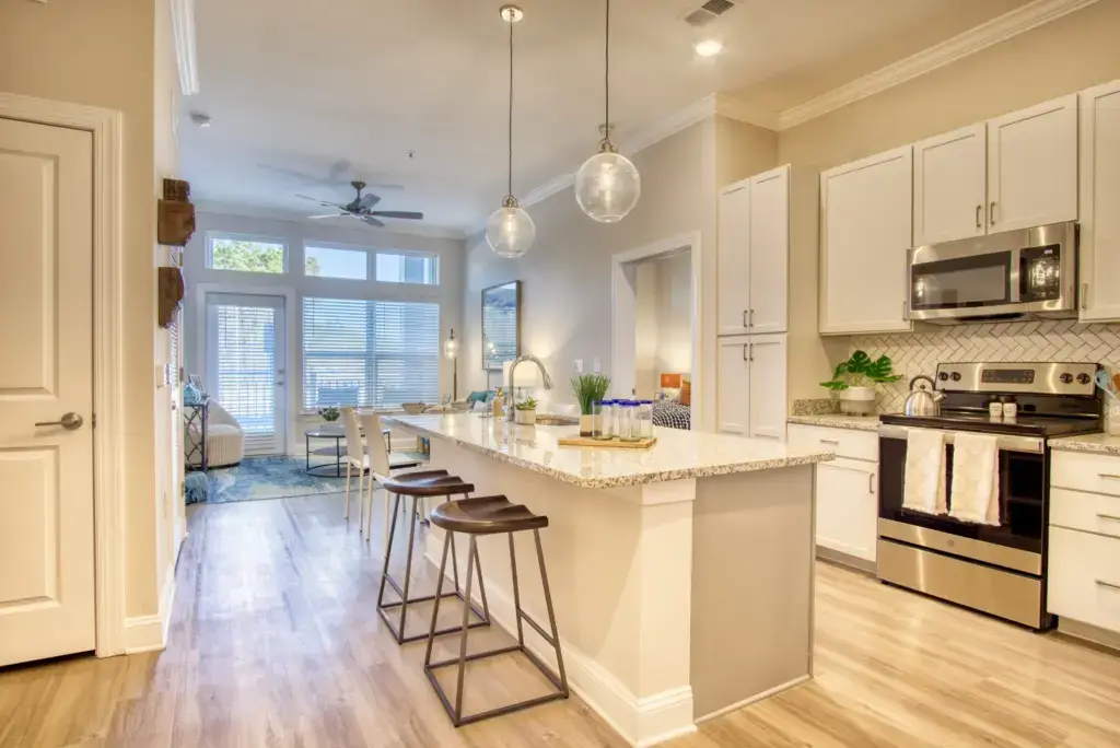Interior View of The Retreat apartments that shows a clean, model kitchen with the living room in distance